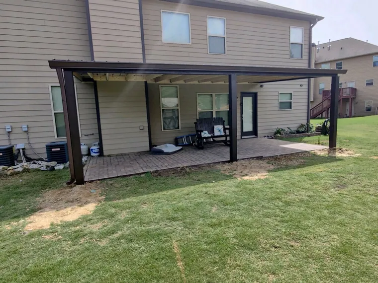 A covered patio with dark posts and beams over a paver patio